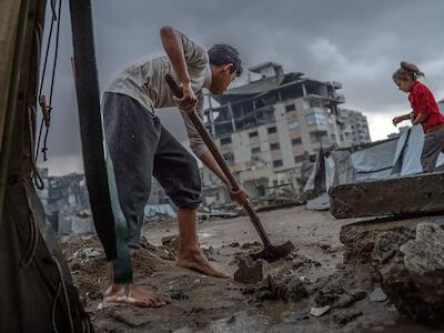 Un niño limpia la entrada de una tienda de campaña tras las fuertes lluvias en Gaza. Foto de WFP/Maxime Le Lijour.