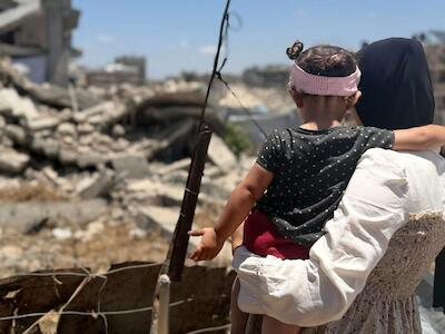UNDP/PAPP Una mujer palestina sostiene a una niña pequeña mientras contempla los escombros en Gaza.