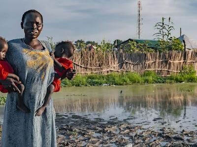 Foto: Una mujer sostiene a sus hijos frente a su casa afectada por las inundaciones en Sudán del Sur. (UNICEF)