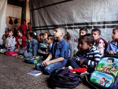 Alumnos sentados en el suelo mientras asisten a clase en una escuela de educación primaria gestionada por la UNRWA. / ONU   