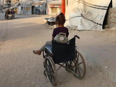 Una niña sentada en la silla de ruedas que utiliza para transportar bidones de agua. © NOUR ALSAQQA/MSF