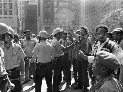 Democracy Now! - Imagen: En 1969 Jesse Jackson (centroderecha, levantando los brazos) lidera una protesta de 4 000 personas contra la discriminación racial en el sector de la construcción (1969). Foto: Gary Settle/The New York Times