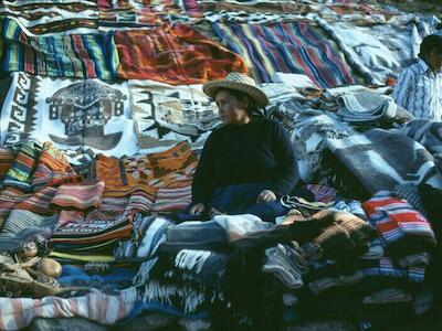Mujer muestra alfombras hechas a mano en una carretera cerca de Cuzco, Perú. Foto de Urbain J. Kinet
