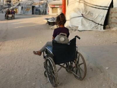 Una niña sentada en una silla de ruedas que utiliza para transportar bidones de agua. © MSF